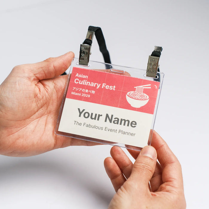 Two hands holding the front of a paper event name badge on a black double-clip lanyard